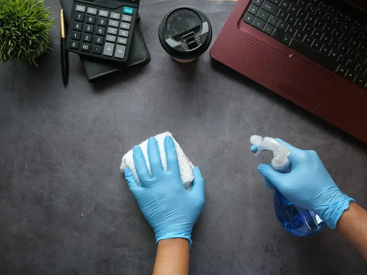 Gloved hands wiping down an office desk
